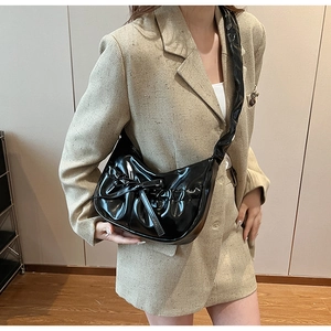 Close-up of a glossy black patent leather shoulder bag with chic bow detail and ruched design