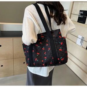 Close-up of black quilted tote bag featuring a vibrant red cherry pattern on canvas