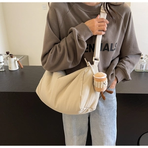 Detail of beige large fabric crossbody bag with wide strap and plush coffee cup charm