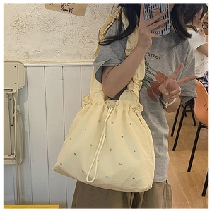 Detail view of yellow nylon drawstring tote bag with silver beads and ruffled shoulder strap
