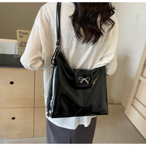 Close-up of black patent leather handbag featuring a silver metal bow and chain detail