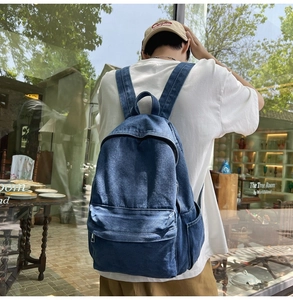 Detailed back view of a dark blue denim backpack with side pockets on a model