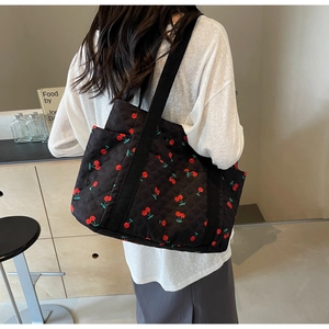 Detail of a black quilted tote bag featuring red cherry patterns and a wide fabric strap