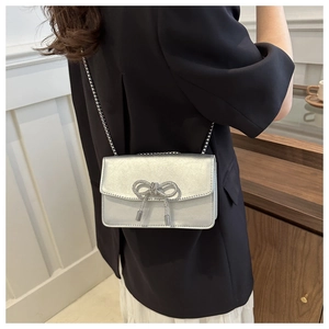 Detail of silver crossbody bag featuring a sparkling rhinestone bow and chain strap