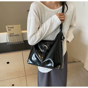 Detail of black glossy PU leather handbag with a silver metal bow buckle and chain strap