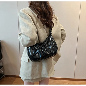 Detail of black PU leather hobo bag featuring pleated design and decorative bow on shoulder strap