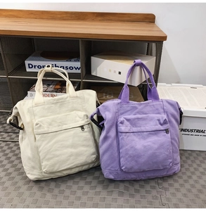 Detail view of canvas tote bags in cream and lilac with front zip pockets and sturdy handles