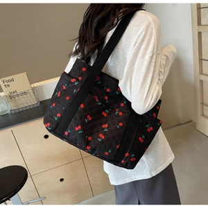 Detailed side view of black quilted tote bag with cherry pattern on a female model