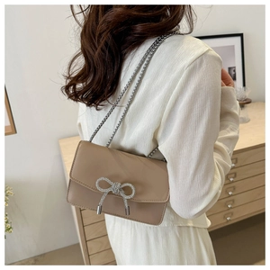 Detail view of khaki PU leather bag featuring a silver rhinestone bow and metal chain strap