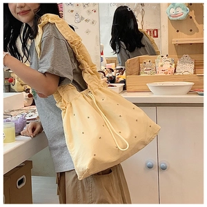 Detail of yellow nylon pleated handbag with pearl embellishments worn by a model
