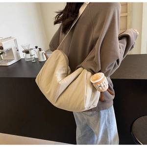 Detail of beige canvas dumpling bag with coffee cup plush pendant on wide strap
