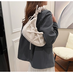 Detail of cream PU crossbody bag with ruffled handle and bow accent on a model