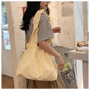 Detail of cream yellow nylon tote bag with drawstring closure and ruffled shoulder strap