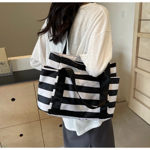 Detail of a black and white striped tote bag with wide shoulder strap worn by a model