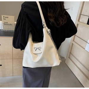 Detail of a creamy white patent leather tote bag with a silver bow and metal chain strap