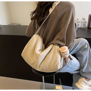 Detail of off-white crescent crossbody bag with a plush coffee cup charm and strap