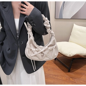 Detail of a creamy PU leather half-moon bag with bow decoration and pleated cloud handle