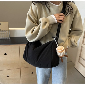 Detail of black crescent nylon crossbody bag featuring a plush coffee cup keychain accessory