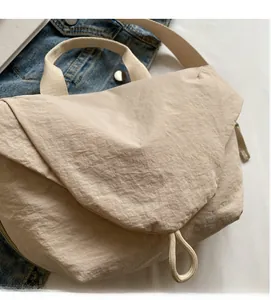 Detail of beige pleated nylon crossbody bag styled on a casual denim jacket