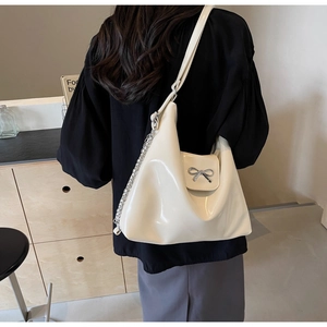 Detail of a creamy white glossy PU leather tote bag with silver bow buckle and metal chain