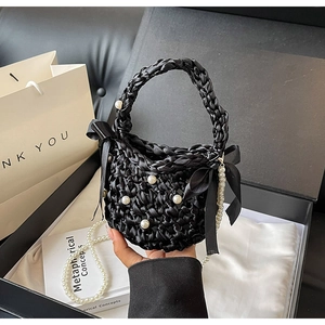 Chic black woven handbag with white pearls and large ribbon bow on a display box