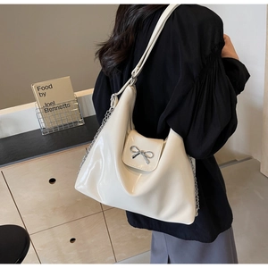 Detail of a creamy white glossy PU leather tote bag with metal bow buckle and chain strap
