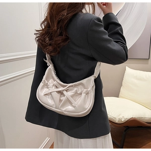 Close-up of cream PU leather shoulder bag with pleated bow detail on model's shoulder