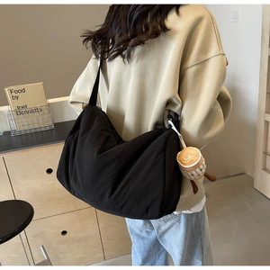 Detail of black canvas half-moon crossbody bag with coffee cup plush pendant on wide strap