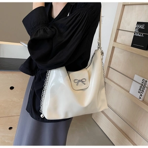 Close-up of creamy white faux leather shoulder bag with silver bow and chain detail