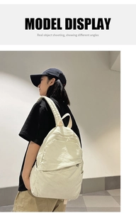 Side view of an oversized off-white canvas backpack worn by a model in casual street style