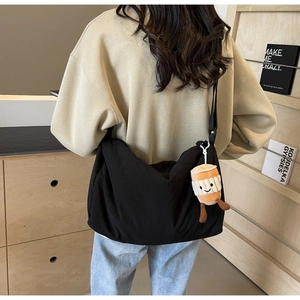 Detail of a black nylon crossbody bag with a coffee cup plush pendant on a soft background