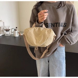 Close-up of a beige crescent crossbody bag worn by a model in a cozy cafe setting
