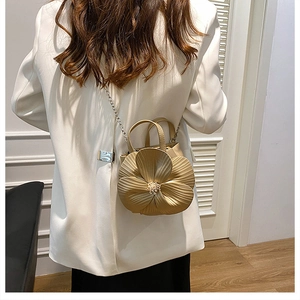 Detail of creative golden flower-shaped crossbody bag with 3D petal design on white suit
