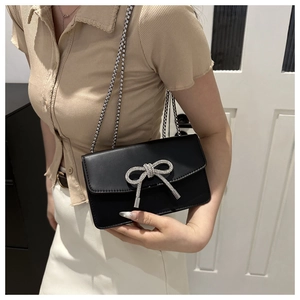 Detail of elegant black PU crossbody bag with silver crystal bow and chain strap