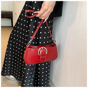 Detail of red PU leather baguette bag with silver buckle held by model in polka dot dress