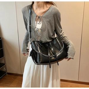 Detail of a black glossy PU leather crossbody bag featuring silver chain and leather tag