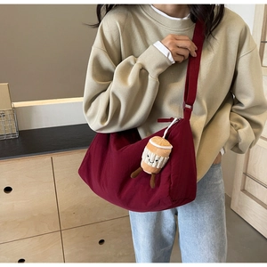 Detail of burgundy crescent crossbody bag with plush coffee cup charm and nylon fabric