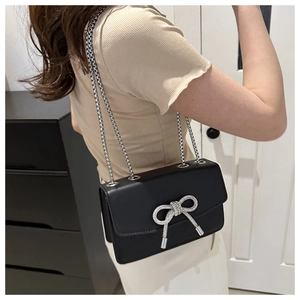 Detail of black PU leather crossbody bag with silver rhinestone bow and metal chain