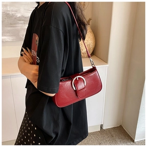 Close-up of deep red glossy PU leather shoulder bag with a large silver metal buckle detail