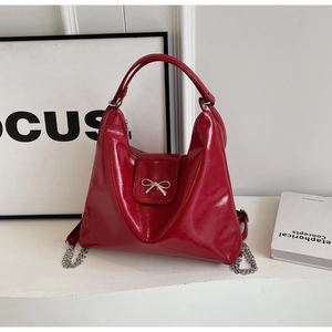 Glossy red PU leather handbag with metallic bow and chain detail on white background