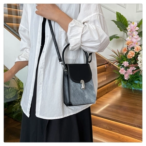 Close-up of black and grey contrast crossbody bag with silver buckle on a wooden staircase