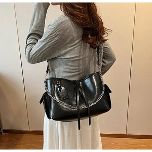 Detail of black glossy PU leather crossbody bag with silver chain and side pocket design
