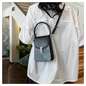 Detail of a black PU leather crossbody bag with silver buckle and top handle shown on model