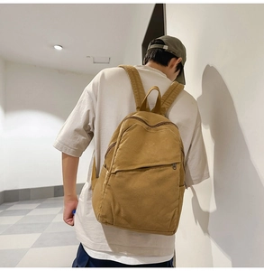 Detailed back view of a mustard yellow canvas backpack worn in a casual indoor setting