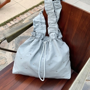 Minimalist light blue nylon tote bag with silver studs and white drawstring on wooden bench