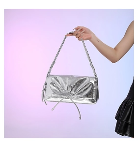 Close-up of metallic silver bow handbag with textured woven strap and glossy finish