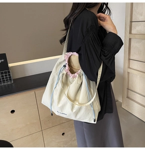 Detail of beige canvas crossbody bag with blue drawstring and pink pleated trim
