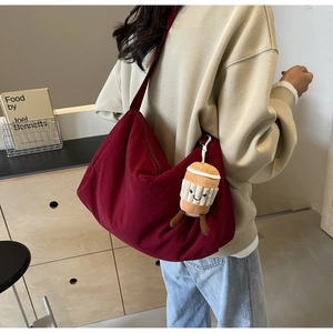 Detail of burgundy nylon crossbody bag with cute plush pendant and adjustable strap