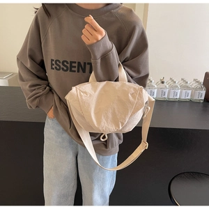 Detail view of a light beige nylon crossbody bag worn by a model in a minimalist cafe