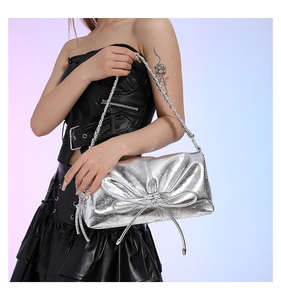 Close-up of a silver metallic shoulder bag with a 3D bow and braided strap on model